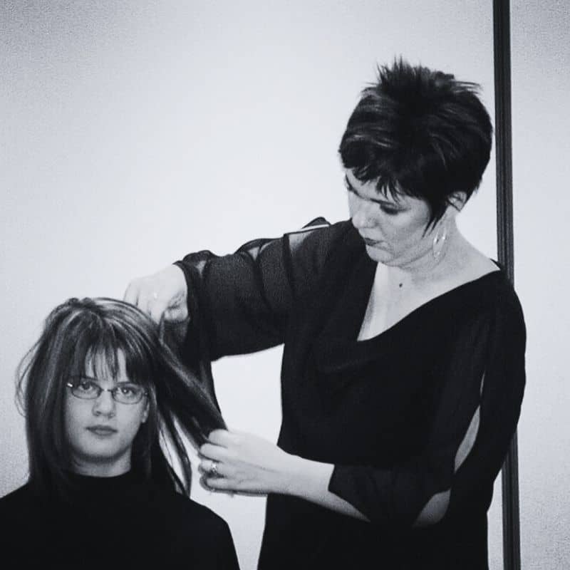 A hairstylist is adjusting the hair of a seated person in a monochrome setting.